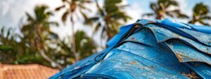 a close-up view of a damaged roof with vibrant tarps and emergency repair tools prominently displayed against the backdrop of a suburban pompano beach home, showcasing the urgency and importance of timely roof repairs.